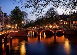 Oświetlone domy i most na kanale w Amsterdamie