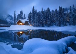 Oświetlony dom w śniegu nad jeziorem Emerald Lake i Góry Skaliste we mgle
