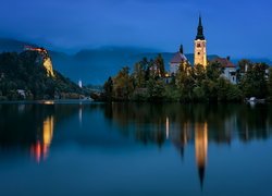 Oświetlony kościół na wyspie Blejski Otok i Zamek Bled w oddali