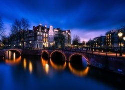 Oświetlony most i budynki nad rzeką w Amsterdamie