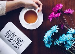 Otwarta książka i filiżanka kawy obok kolorowych kwiatów