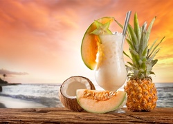 Owocowy koktajl w szklance obok egzotycznych owoców na plaży