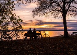 Para na ławce pod drzewami nad jeziorem o zachodzie słońca