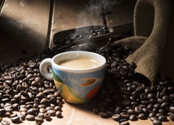Parująca kawa w filiżance obok worka z ziarnami