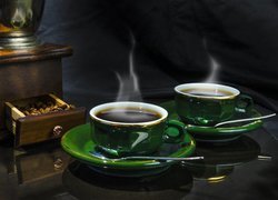 Parująca kawa w filiżankach obok młynka do kawy