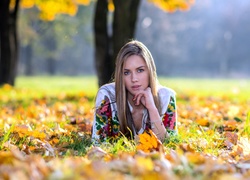 Piękna kobieta pozuje wśród jesiennych liści na łące