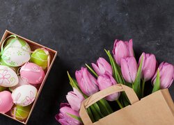 Pisanki w pudełku obok tulipanów w papierowej torbie