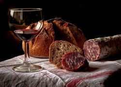 Podsuszana kiełbasa i chleb leżące obok kieliszka z winem