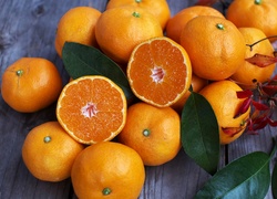 Pomarańcze ułożone na drewnianym blacie wśród liści