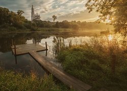 Pomost na jeziorze z widokiem na cerkiew pośród drzew