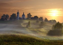 Poranna mgła nad łąką i cerkwią na wzgórzu