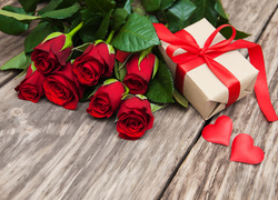 Prezent i małe serduszka obok bukietu czerwonych róż