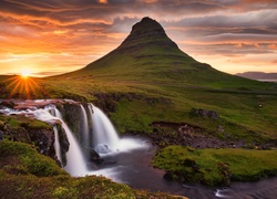 Promienie słońca nad wodospadem Kirkjufellsfoss z widokiem na górę Kirkjufell