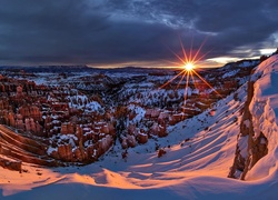 Promienie słoneczne oświetlają kanion zasypany śniegiem