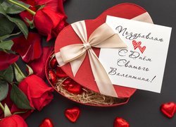 Pudełko czekoladek w kształcie serca obok czerwonych róż