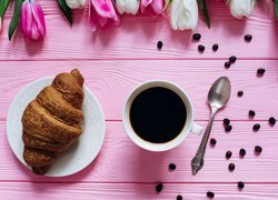 Rogalik croissant z filiżanką kawy i kwiatami