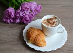 Rogalik na talerzyku obok filiżanki kawy