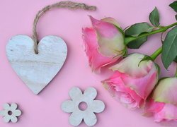 Róże obok drewnianego serca na różowym tle