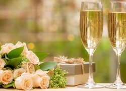 Róże obok prezentu i kieliszków z szampanem
