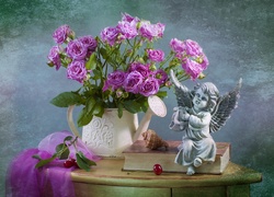 Róże w konewce obok figurki aniołka na książce