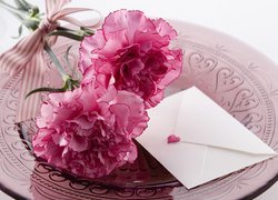 Różowe goździki obok koperty z serduszkiem