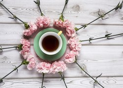 Różowe goździki wokół filiżanki herbaty na desce