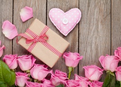 Różowe róże, prezent i gałgankowe serce w kompozycji na deskach