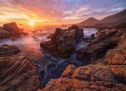 Rozświetlone blaskiem zachodzącego słońca skały na wybrzeżu morza