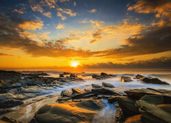 Rozświetlone blaskiem zachodzącego słońca skały w morzu