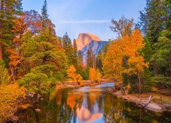 Rozświetlone jesienne drzewa nad rzeką Merced i góra Half Dome w tle