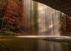 Rozświetlony wodospad spadający ze skały na tle jesiennych drzew
