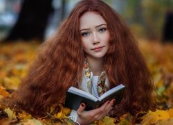 Rudowłosa dziewczyna z książką w jesiennych liściach