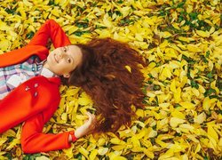 Rudowłosa kobieta leżąca na pożółkłych liściach