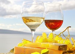 Ser i winogrona obok kieliszków z winem na tle rozmytego nieba