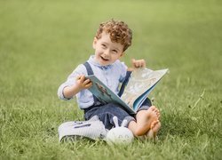 Siedzący na trawie chłopczyk z otwartą książką