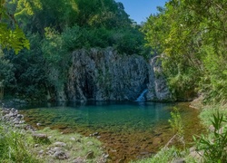 Skalny wodospad wśród zieleni i drzew wpada do kamienistego jeziora