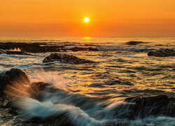 Skały i fale w blasku zachodzącego słońca nad morzem