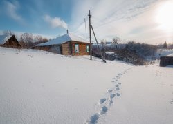 Ślady w śniegu obok zaśnieżonych drewnianych domów