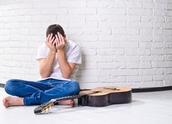 Smutny mężczyzna z gitarą oparty o ścianę