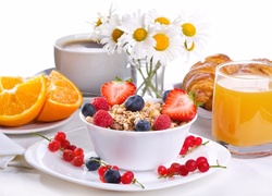 Sok obok miski z płatkami i owocami, kawa i rogaliki podane na śniadanie