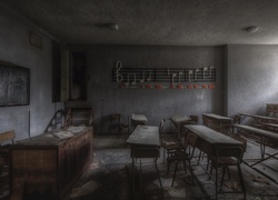 Stara zaniedbana szkolna klasa z ławkami, tablicą i nutami na ścianie