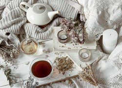 Suszone kwiaty i filiżanka herbaty obok czajnika i świec