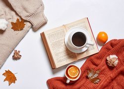 Swetry obok filiżanki kawy na otwartej książce