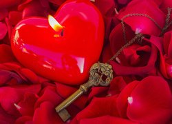 Świeca w kształcie serca obok klucza na płatkach róż