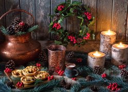 Świece w drewnianych świecznikach obok wieńca świątecznego i gałązek