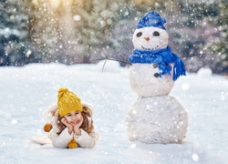 Szczęśliwa dziewczynka na śniegu obok bałwanka
