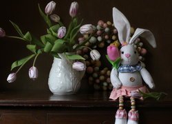 Szmaciany zając obok wieńca z jajek i tulipanów w wazonie