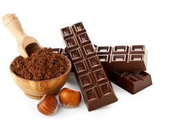 Tabliczki czekolady obok miseczki kakao i orzechów laskowych