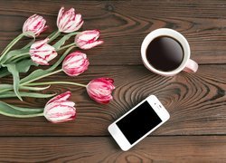 Telefon obok filiżanki z kawą i tulipanów na deskach