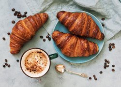 Trzy croissanty na talerzu obok kubka z kawą